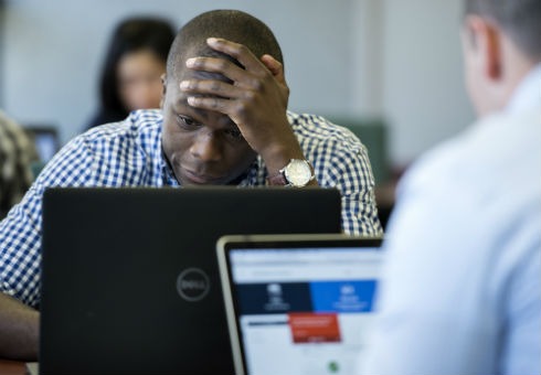 A student concentrates with head in hand in front of his laptop