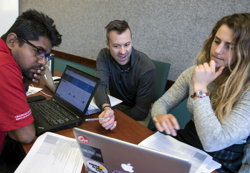 Three students work around a computer during the hackathon