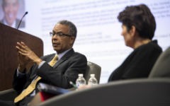 Aaron Williams gestures while he speaks seated in a chair on stage