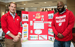 Two Wisconsin MBA students stand by a poster showcasing their startup