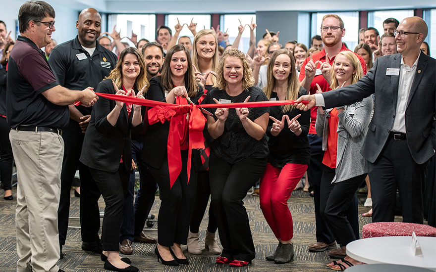 Jamie Macias preparing to cut a red ribbon with a group of people around her