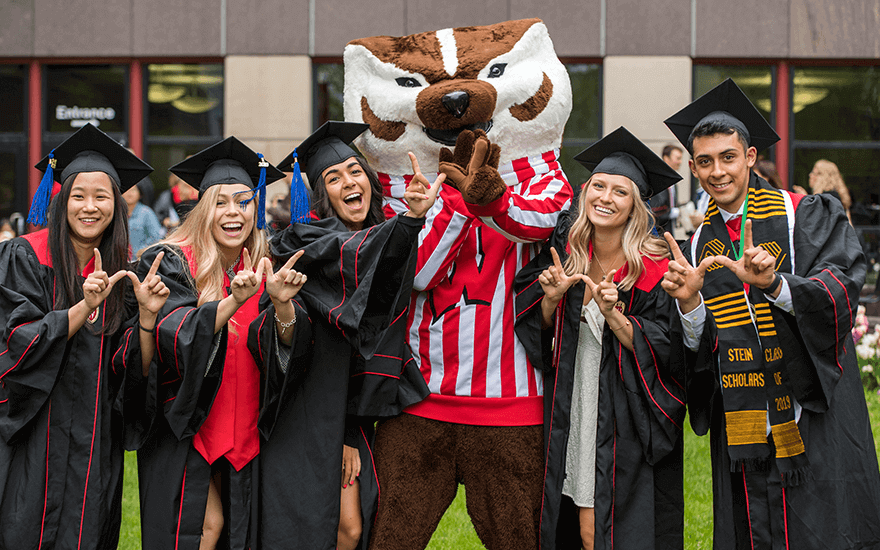 Undergraduate students wearing graduation robes posing with mascot Bucky Badger