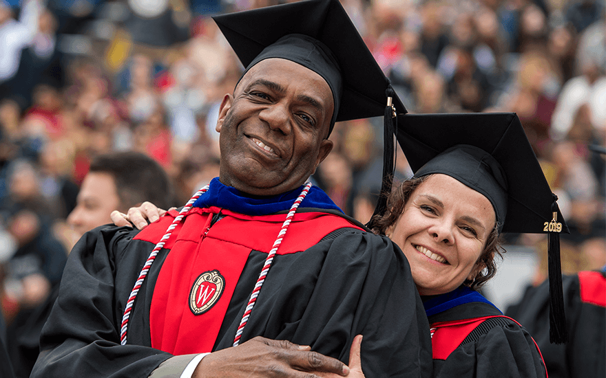 A man and woman wearing graduation robes with 2019 pin on their hats