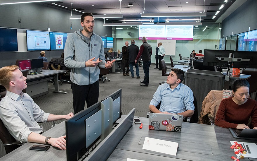 Three undergraduate students listen to an MBA student in the Finance and Analytics Lab