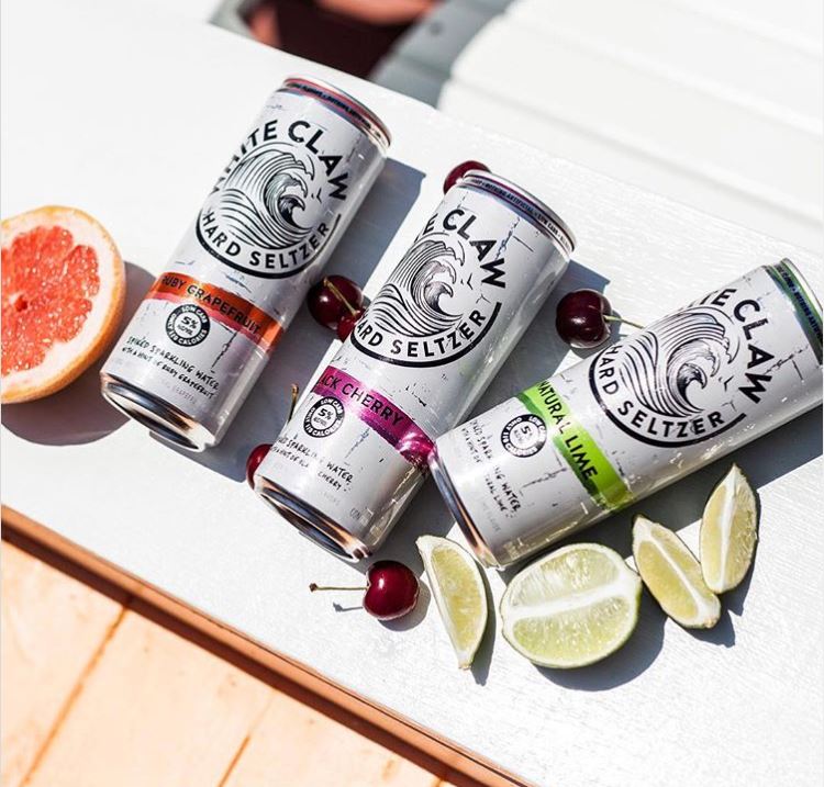 Three White Claw cans with lime and grapefruit slices and cherries aroun