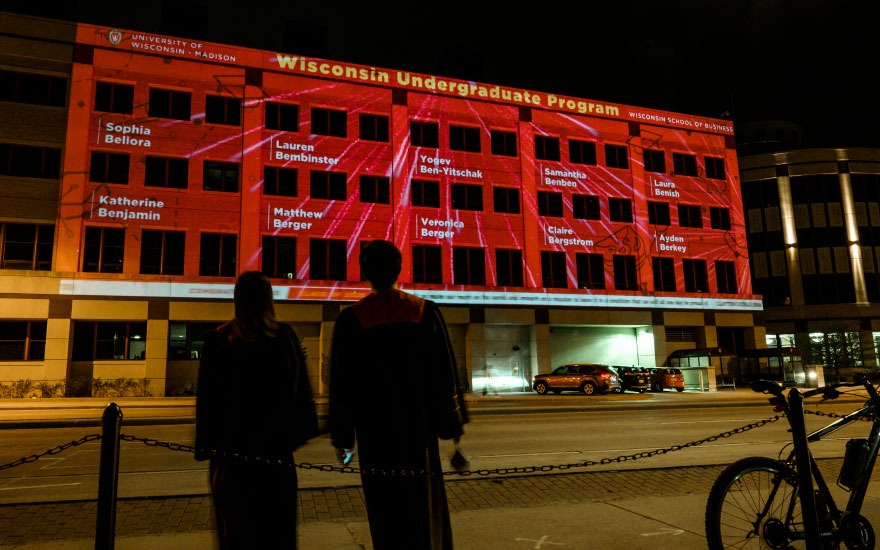 students in graduation gowns looking at names on Grainger Hall