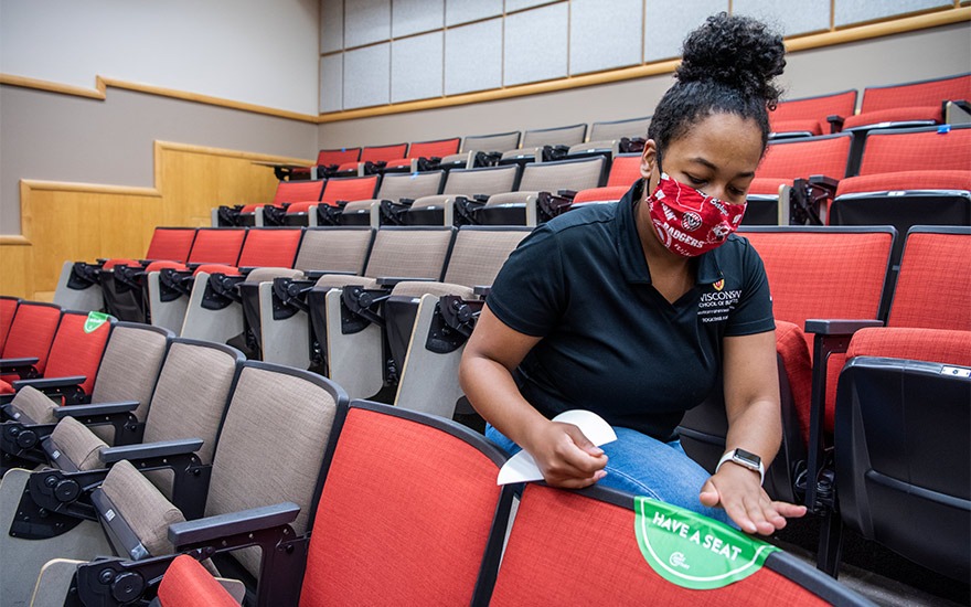 A student worker placing stickers on chairs in Grainger Hall