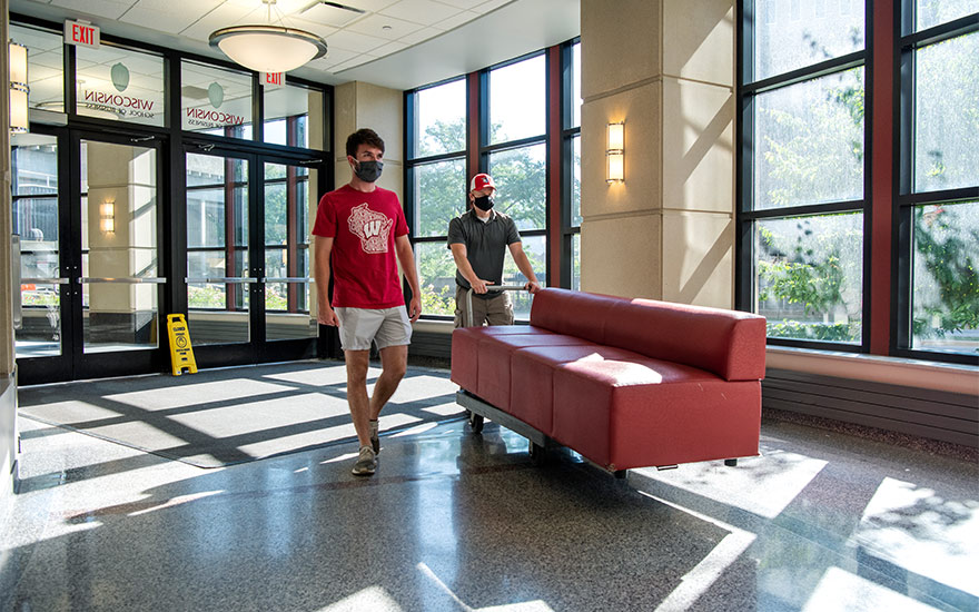 Two men moving a sofa in a common area of Grainger Hall