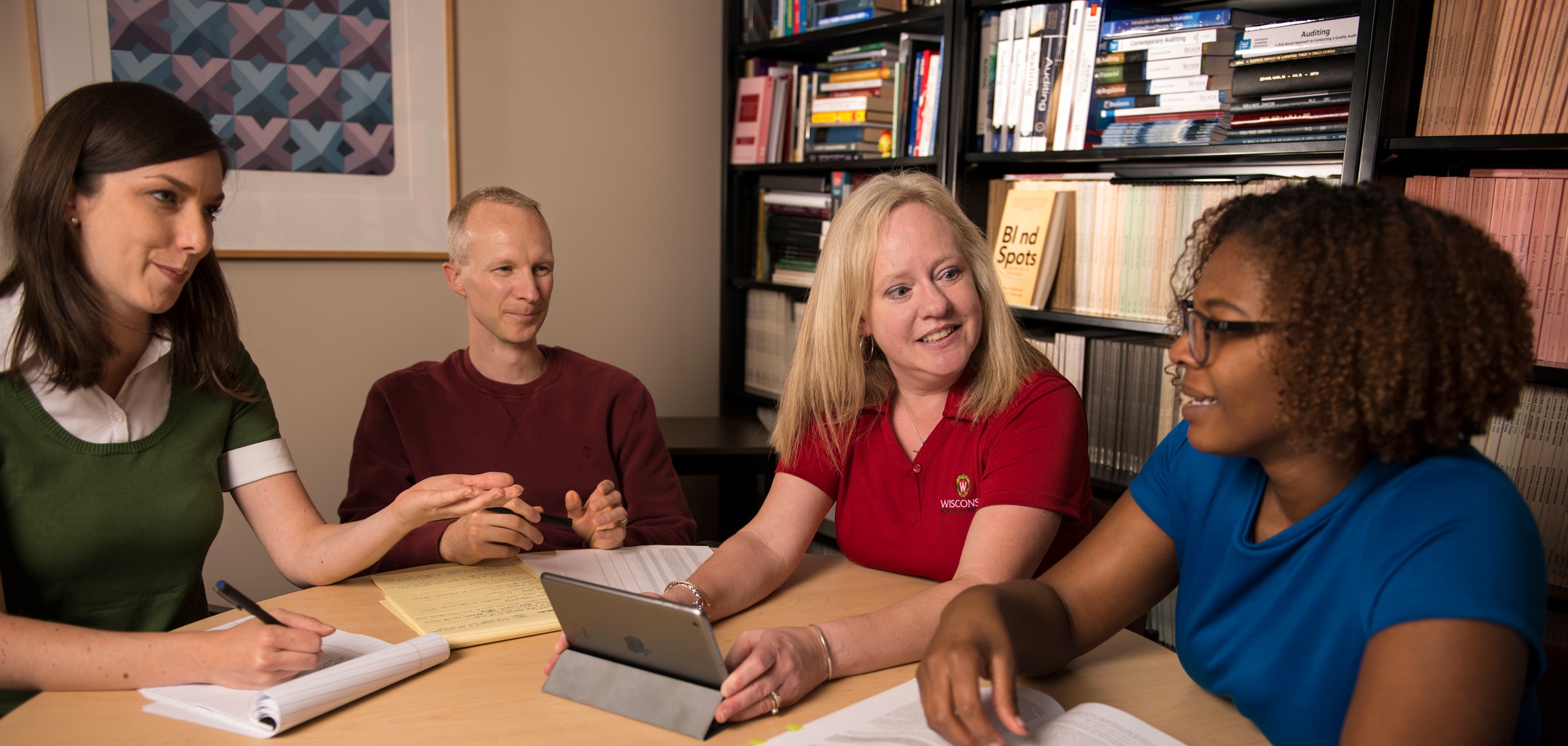 One man and three women gathered around a table talking to each other