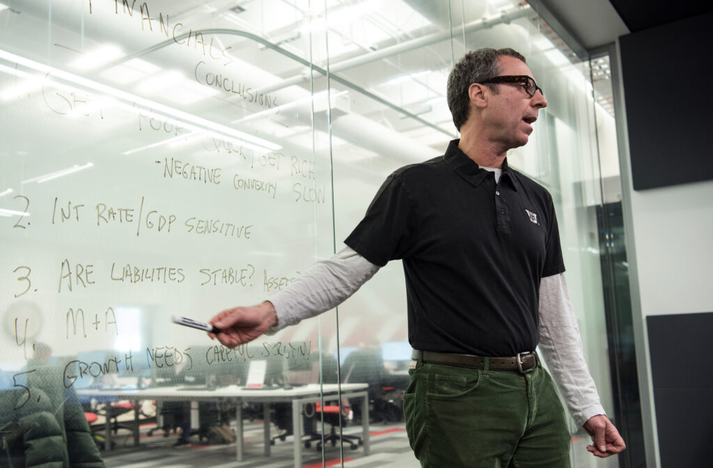 A professor pointing to writing on the board behind him