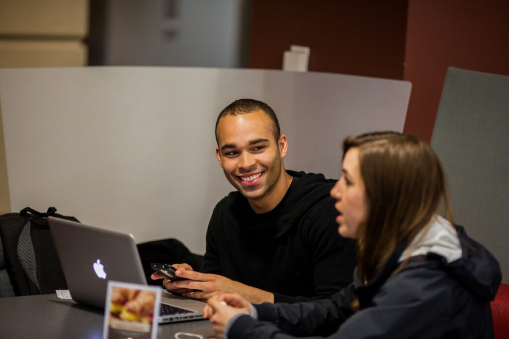 Two students talking and working at a laptop