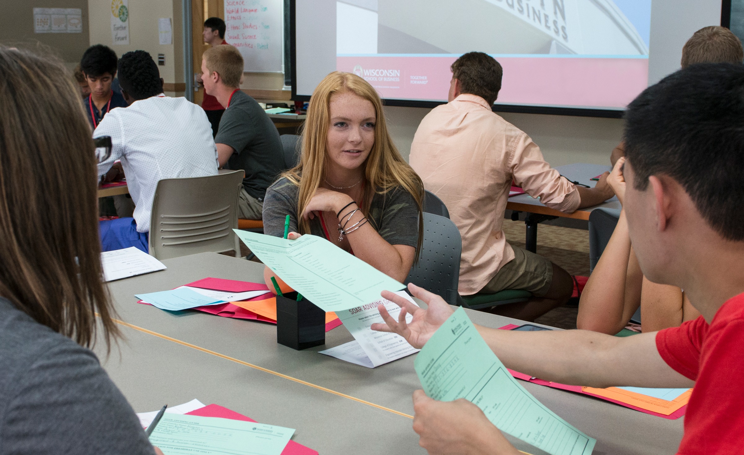 A woman handing out papers to students sitting at a table