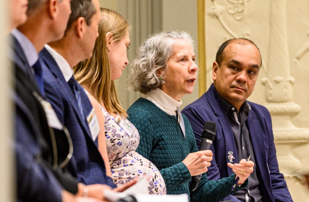 A panel of three men and two men with one woman holding and using a microphone to talk