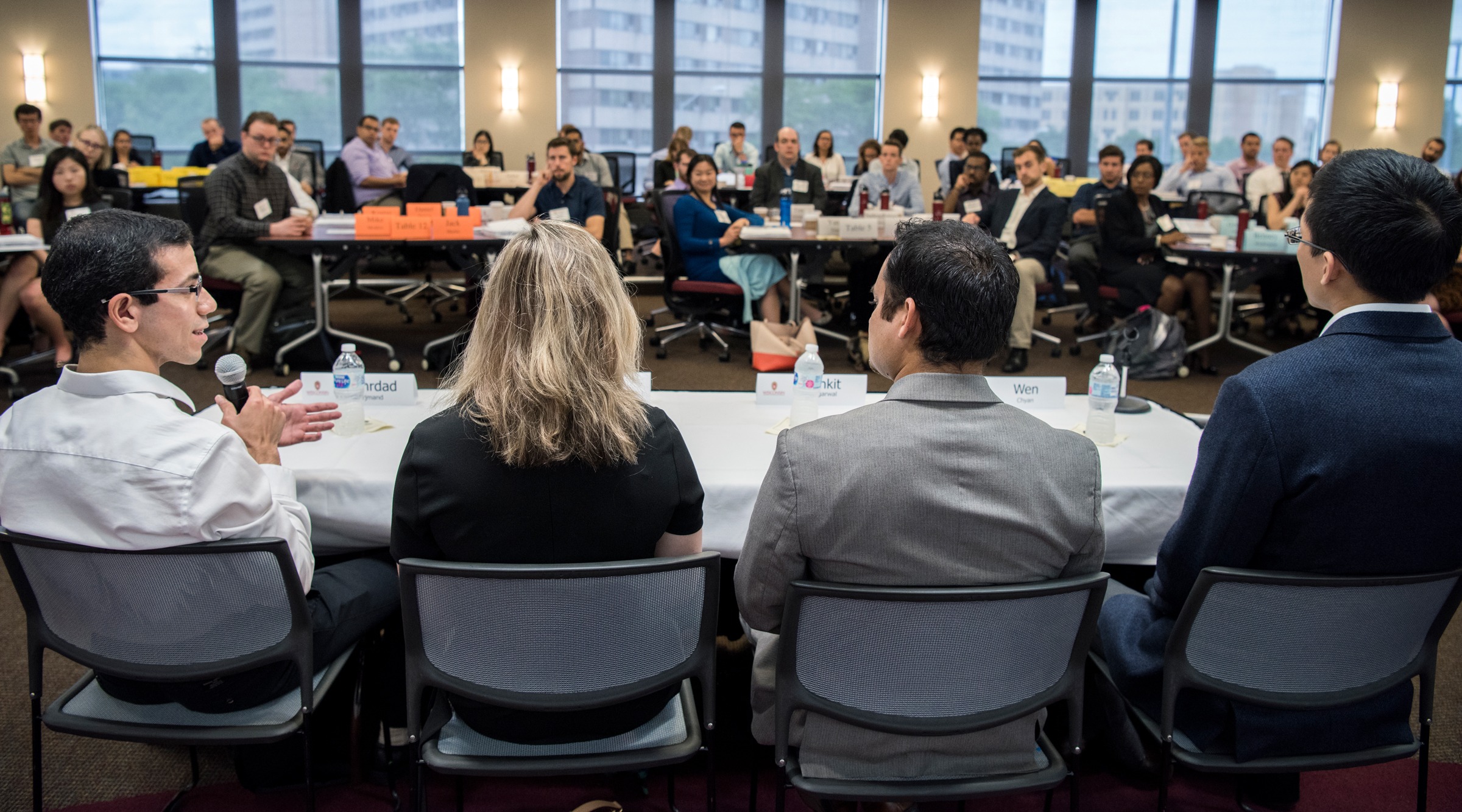 Three men and one woman talking to a room full of people at an event