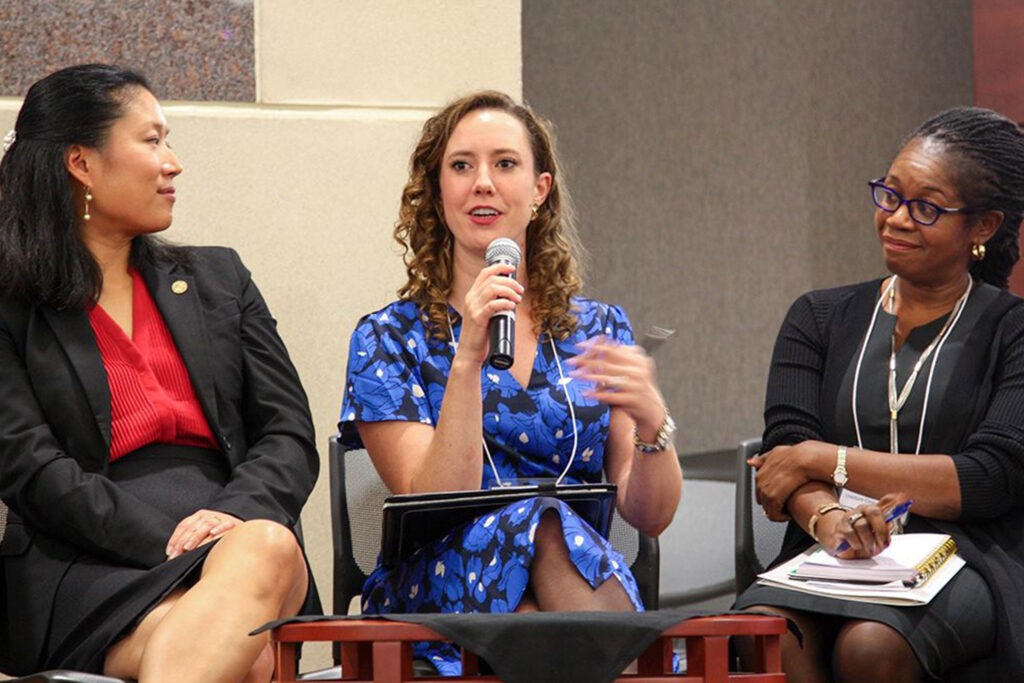 Three women sitting with the middle woman talking through a microphone in her hand