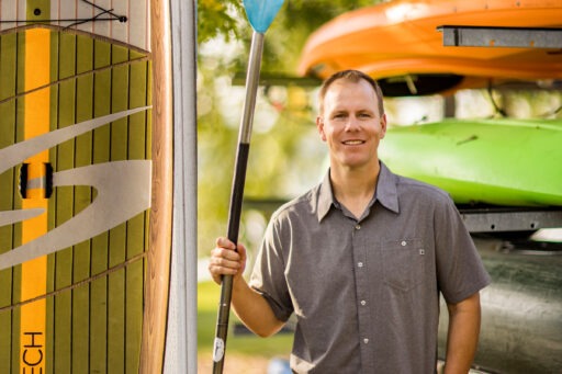 Tyler Leeper holds a paddle in front of some kayaks