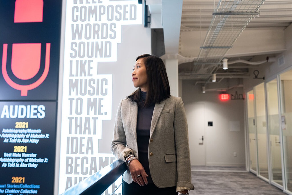 Cynthia leaning at the railing in front of art that says "Well composed words sound like music to me. That idea became audible."