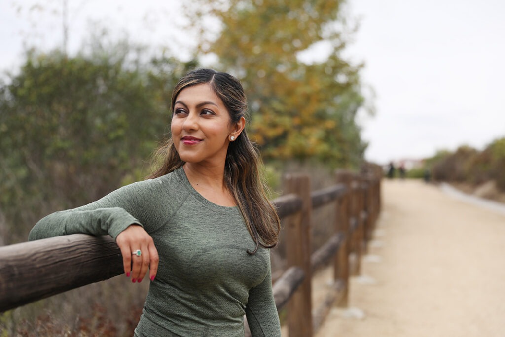 Reena leaning against a fence along a trail
