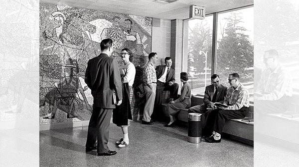 Seven students talking in a room with three sitting on a bench and the rest are standing