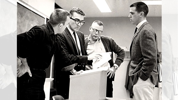 A professor talking with three students around a podium