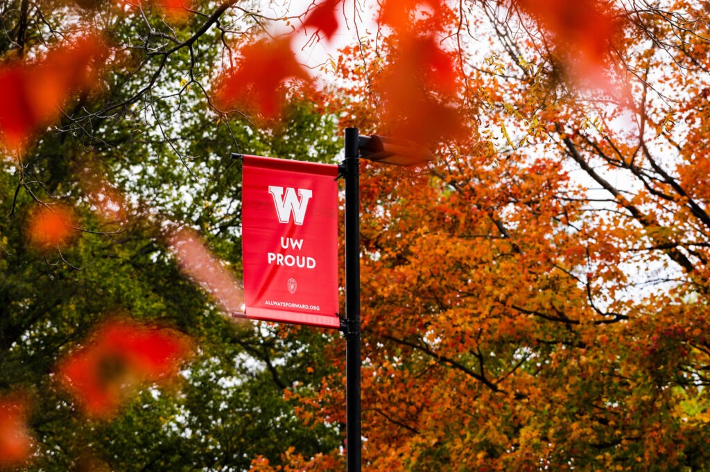 photo of UW Proud flag in front of autumn trees