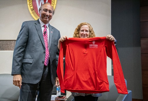 Chancellor Mnookin holds up a red fleece WSB pullover gift as she stands next to Dean Samba on stage