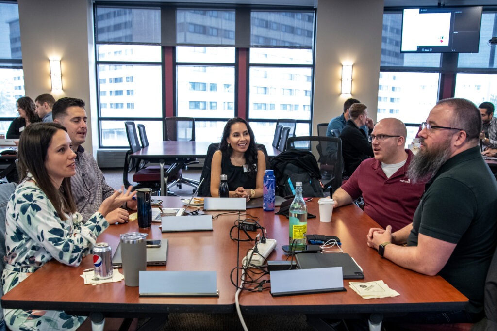 A group of two women and three men are sitting a desk and having a discussion