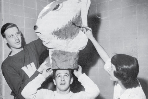 Black and white photo of Bill Sachse and Connie Conrad assisting Bill Sagal with their handcrafted Bucky Badger head.