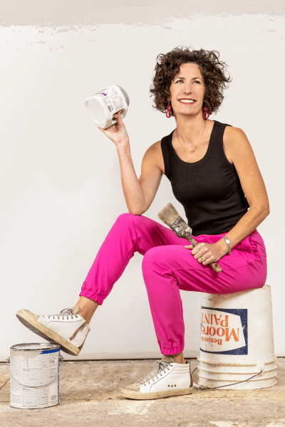 Lindsey Uselding sitting on paint bucket and holding paint brush