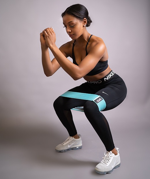 Jayla, a Black woman in athletic wear, performs a squat with a resistance band on her thighs