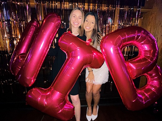 Kenzi and a fellow member of Women in Business are holding large pink balloons at an engagement event