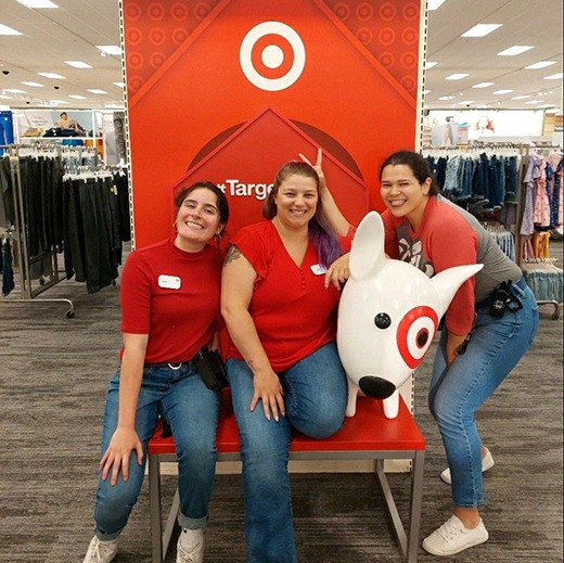 Angie sitting on a red Target chair with a friend and another friend standing next to them with the Target dog mascot