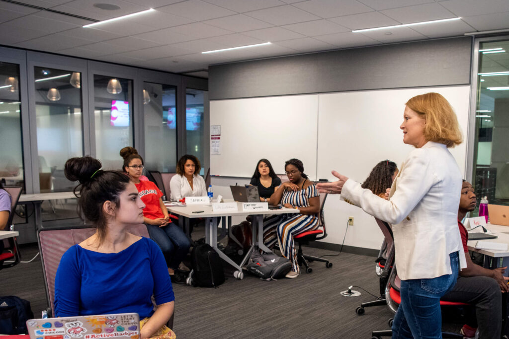 A woman teaching a class to students who are sitting at desks.