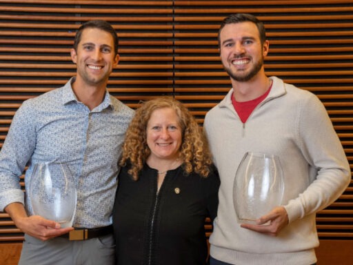 Tyler Kennedy and Wes Schroll holding glass containers with a woman standing between them