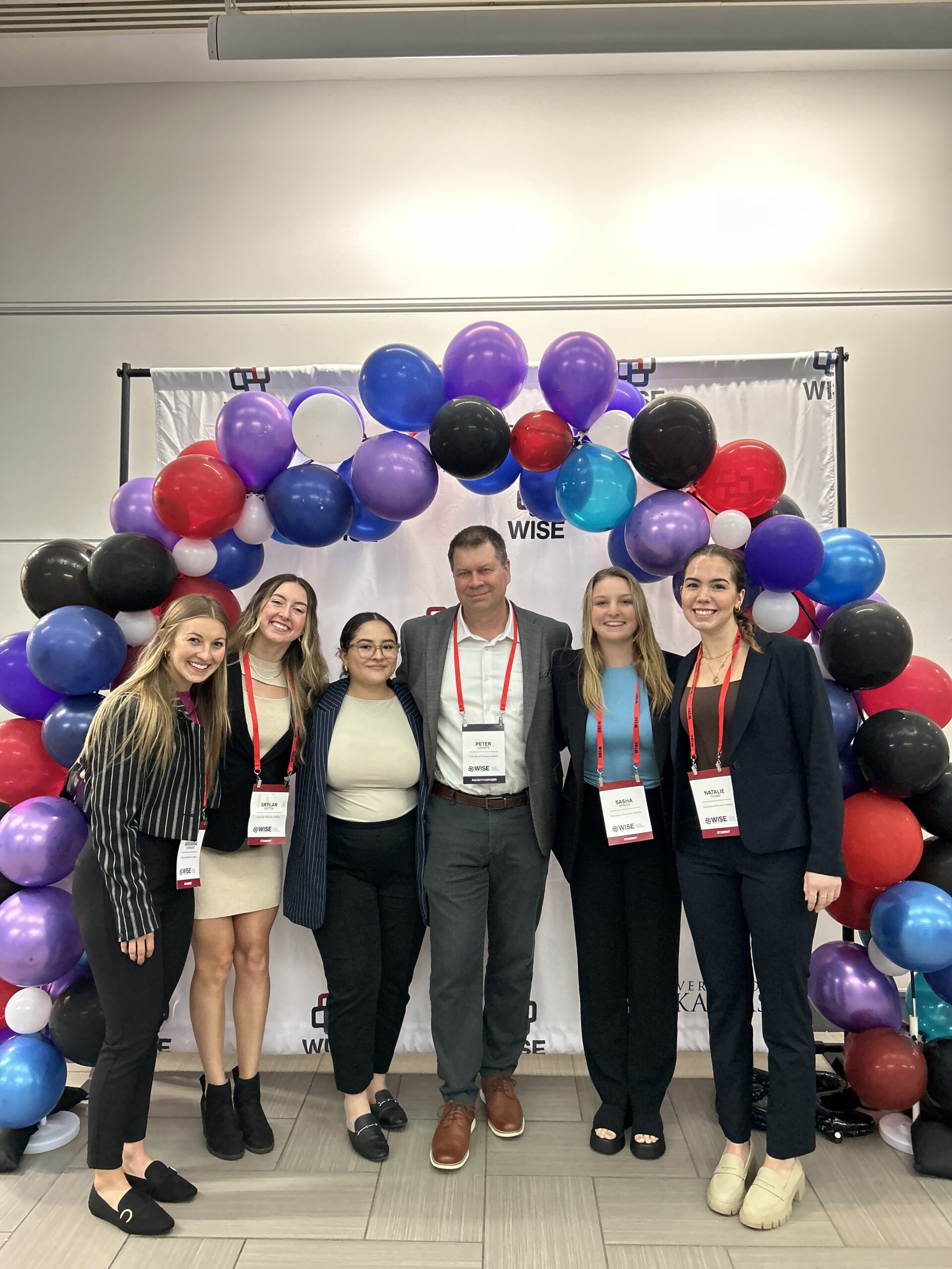 Breanna Schneider, Skylar Rotter, Sasha Kryazh, Natalie Thoms, Brenda De La Torre, and Peter Lukszys standing under a balloon arch.