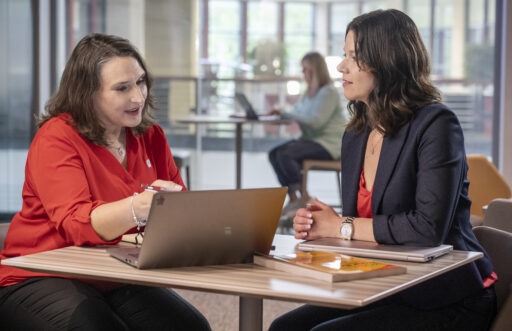 An executive MBA student sits at a table with her coach, who points to her laptop