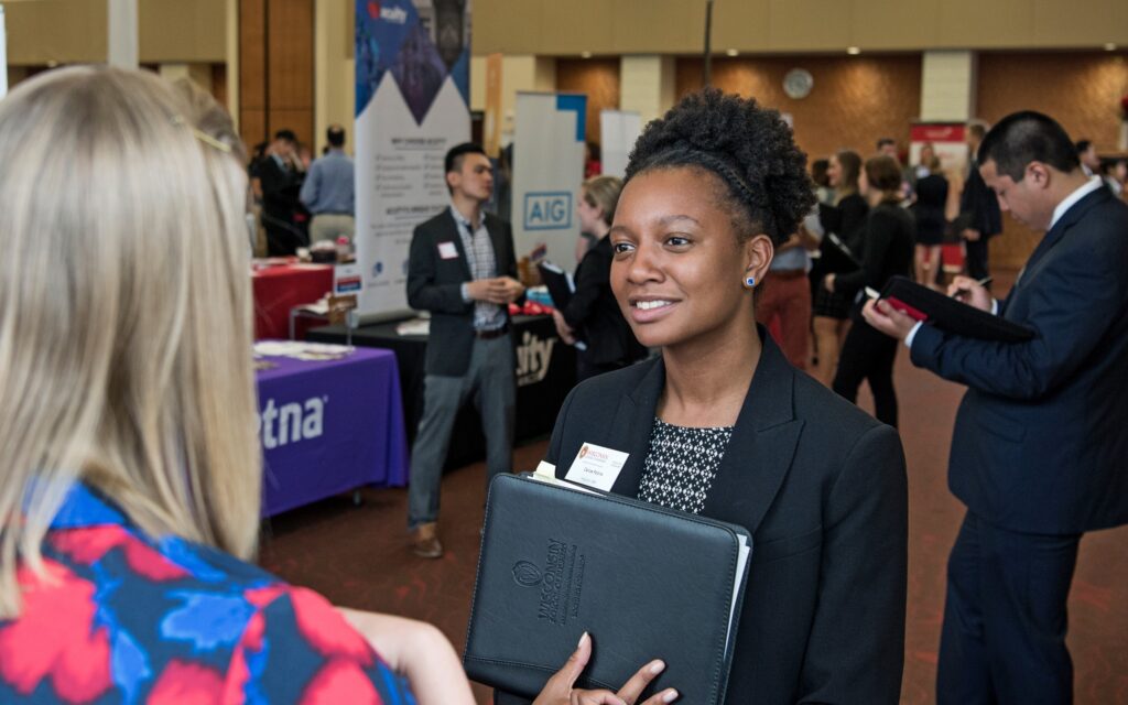 A student holds her portfolio and speaks with a recruiter at a job fair