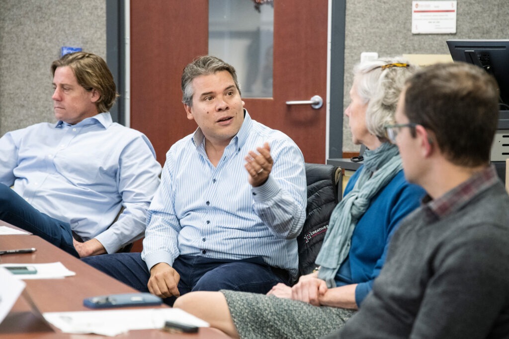 Four professors sit at a table while one of them talks