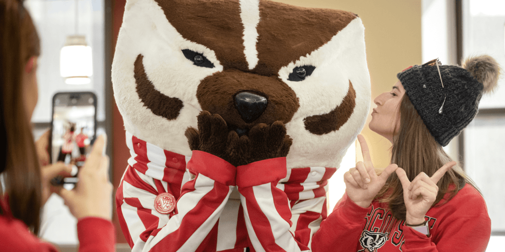 A woman posing with her fingers in a W next to Bucky Badger