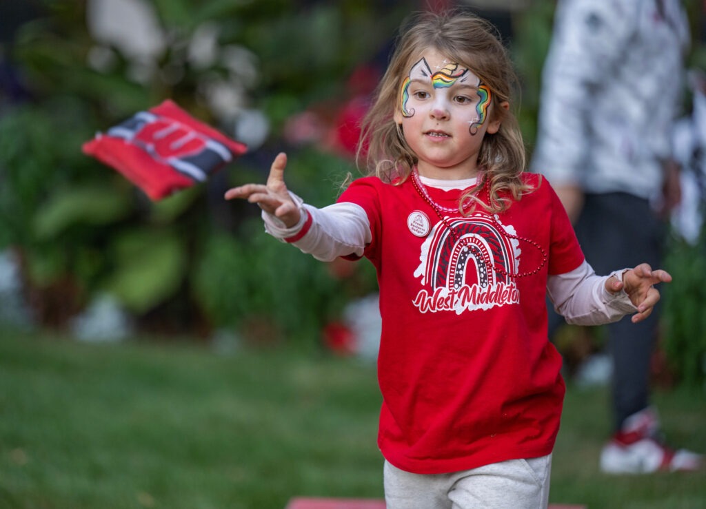 Sporting festive beads and colorful face paint, Nora Meck tosses a bean bag during a rousing game of cornhole with her little brother in Grainger Hall’s courtyard. 