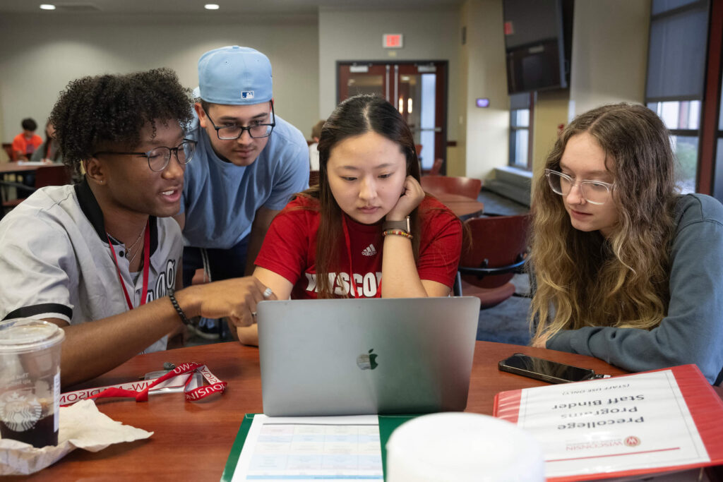 Four students at a desk looking at a laptop screen.