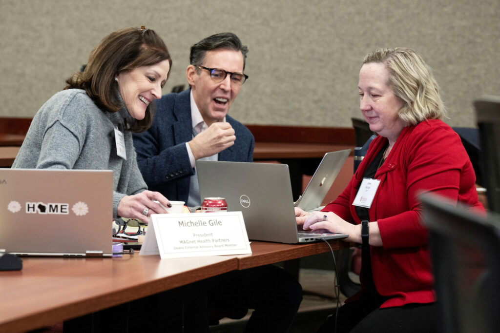 three board members sit at a table with a shared laptop in front of them