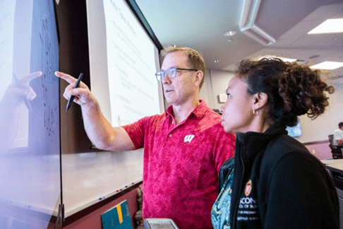 UW Professor explaining concepts on white board to an MBA student