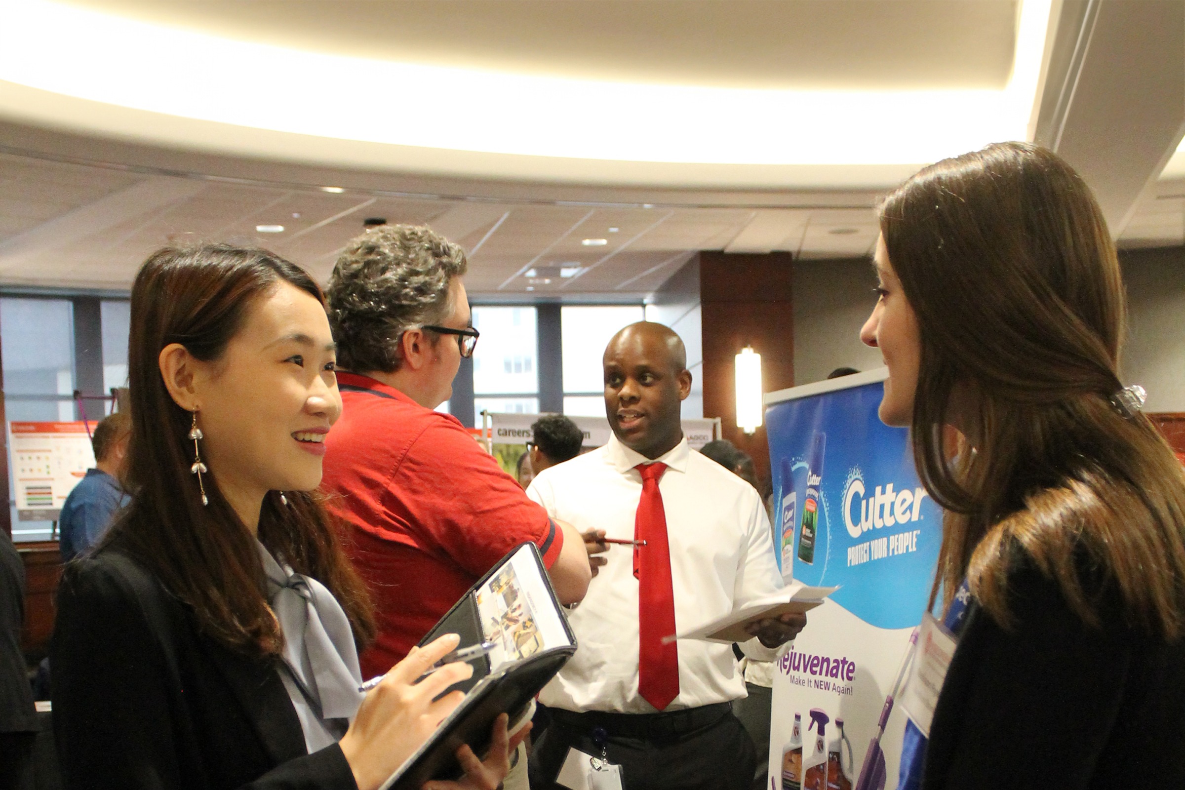 People are standing at an event with two women talking to each other and two men talking to each other in the background.