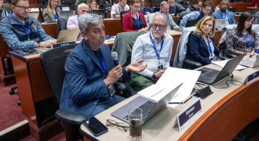 Mentor Naveen Agarwal speaking with microphone and sitting among many other mentors in an auditorium during during a recent Creative Destruction Lab session.