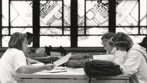 a black and white photo of students working and studying at tables with Grainger Hall's Library Window in the background