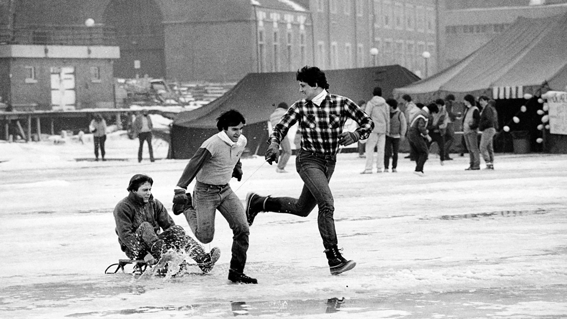 A man sledding on the lake with two other men running along side him.