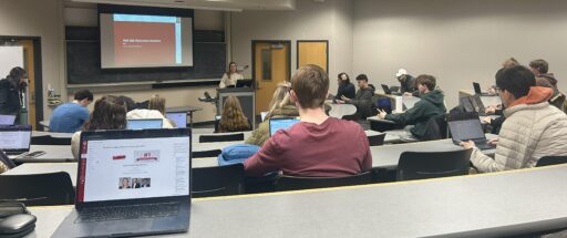 A photo of Caroline in front of the classroom, leading a discussion with students seated in rows.