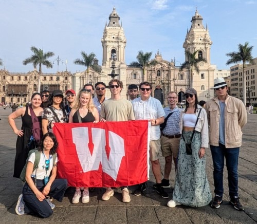 Wisconsin MBA students pose with the Motion W flag in front of buildings and palm trees in Lima, Peru.