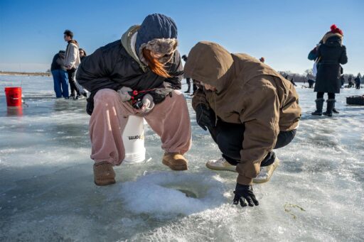 A student and his friend peer into the hole in the ice